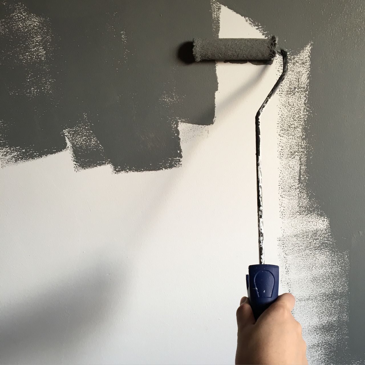 Een hand brengt verf aan met een roller op een muur