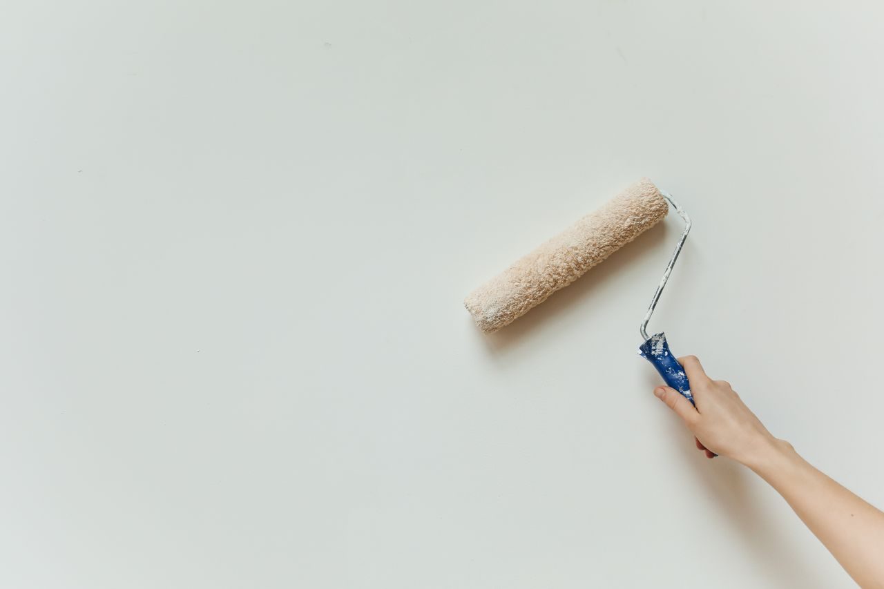 Een schilderende hand en een roller bij een lichte muur